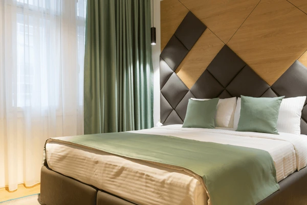 A cozy, elegant bedroom with soft green blackout curtains and sheer white layers ideal for cooling Dubai homes in summer.