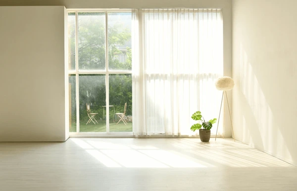 Minimalist living room with sheer white curtains, large floor-to-ceiling windows, a potted plant, and a cozy standing lamp, creating a sleek and airy Dubai home.