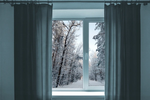 Modern grey curtains framing a large window with a snowy winter forest view outside, creating a cozy and elegant ambiance.