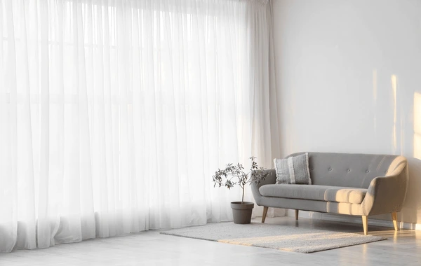 Minimalist living room in Dubai 2025 with elegant white sheer curtains, a gray sofa, and natural sunlight.