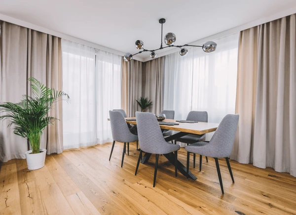 Elegant dining room with wooden table, gray chairs, and stylish layered hanging curtains in a Dubai home.