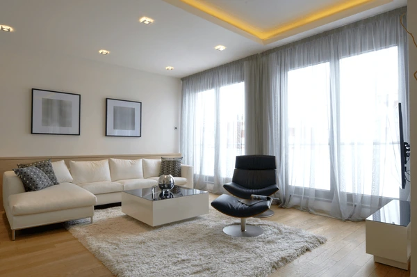 Modern living room with sheer white green wall curtains, white sofa, black lounge chair, and cozy contemporary décor in Dubai 2025.