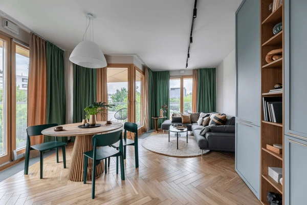 Modern open living and dining room with elegant green long curtains, wooden flooring, and stylish furniture in Dubai 2025.