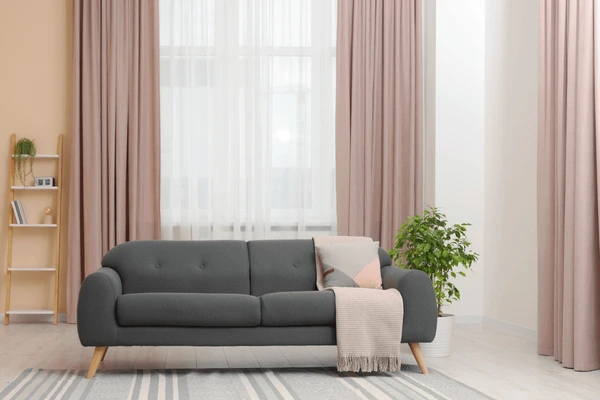 Stylish living room in Dubai with blush pink long curtains, a grey sofa, indoor plant, and minimal modern décor.