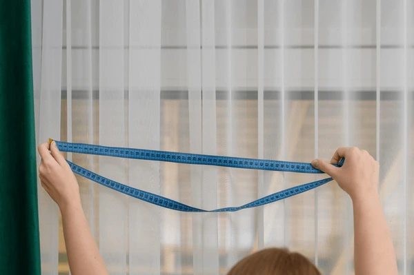 Worker measuring window with a tape for normal sized short curtains installation in Dubai.

