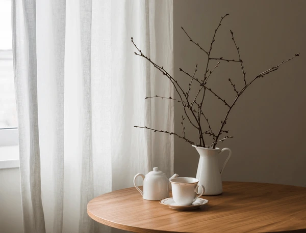 Soft white linen easy-to-dry curtains beside a wooden table with tea set and dried branches, creating a calm and modern Dubai home interior.