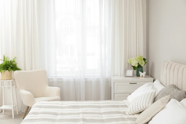 Best Easy-To-Dry Curtains in Dubai 2025 featuring soft white drapes in a bright cozy bedroom with beige furniture, green plants, and a serene modern aesthetic.