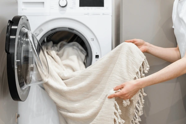 A person unloading beige tassel curtains from a washing machine, showcasing machine-washable luxury curtains ideal for modern Dubai homes.