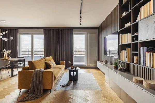 Best Measured Curtains in Dubai 2025 featuring dark brown drapes in a contemporary living room with mustard sofa, wooden floors, and elegant shelving for cozy, modern homes.