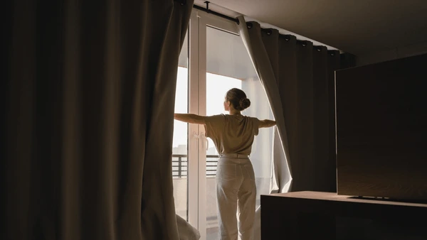 Woman opening thick Best Blackout Curtains in a modern bedroom during sunrise, showcasing luxurious Christmas-ready blackout curtains in Dubai 2025.