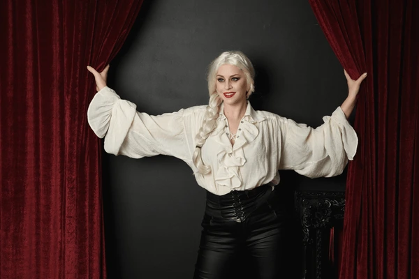 Stylish woman with platinum hair standing between rich red velvet Halloween curtains, creating a glamorous gothic and luxurious interior setting in Dubai 2025.
