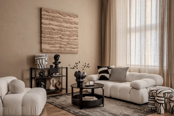 A chic modern living room in Dubai featuring beige textured curtains, sculptural wall art, cozy white sofas, and black minimalist decor — reflecting November’s top trending curtain style.