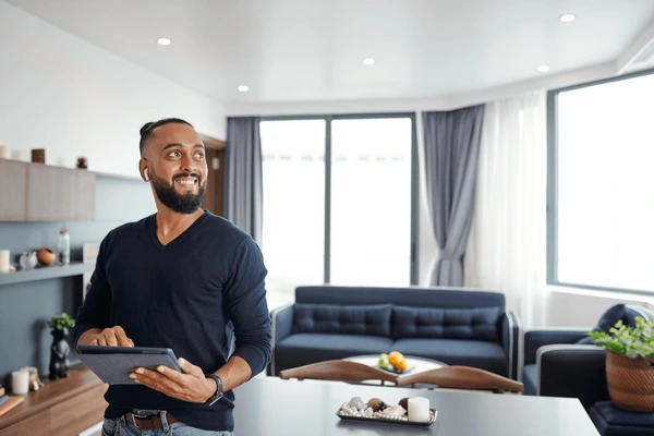 Smiling man using a tablet in a stylish Dubai apartment with elegant blue motorized smart curtains and contemporary furniture.